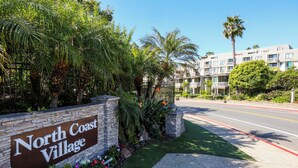 A sign for North Coast Village with a road in front and a building in the background. - Harbor & Ocean View Coastal Retreat – Walk to Beach & Marina (Oceanside)