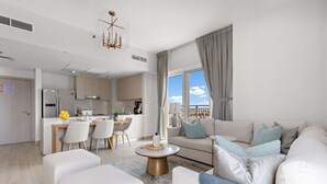 A modern living room with a sofa, ottomans, and a coffee table. There is a dining area with chairs and a table, and a kitchen in the background. - Silkhaus Lavish 3BR Maid Yas Island (Abu Dhabi)
