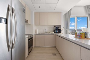 A modern kitchen with light wood cabinets, stainless steel appliances, and a view of the sky through a large window. - Silkhaus Lavish 3BR Maid Yas Island (Abu Dhabi)