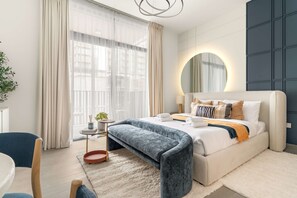 A modern bedroom with a bed, bedside table, bench, and a large mirror. - Silkhaus Chic Studio Sobha Hartland Kensington (Dubai)