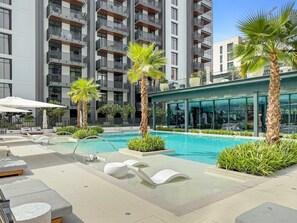 Un hôtel moderne doté d’une piscine, de chaises longues et de palmiers.