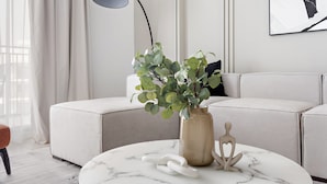 Ein modernes Wohnzimmer mit einem runden Couchtisch aus Marmor, einer beige farbenen Vase mit Grünpflanzen und einer schwarzen Stehlampe.
