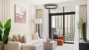 A modern living room with a sofa, coffee table, and a view of tall buildings through large windows. - Silkhaus Luxurious 1bdr Palace Residences (Dubai)