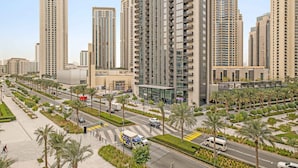 A high-rise residential building with a modern architectural design, featuring multiple balconies and a well-maintained surrounding landscape with palm trees and a pedestrian pathway. - Silkhaus Luxurious 1bdr Palace Residences (Dubai)