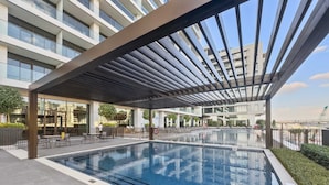 A modern outdoor pool area with a covered seating area and a view of the cityscape. - Silkhaus Luxurious 1bdr Palace Residences (Dubai)