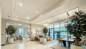 A spacious lobby with a polished marble floor, comfortable seating areas, large windows offering a view of the outside, and several potted plants. - Silkhaus Luxurious 1bdr Palace Residences (Dubai)