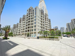 Ein modernes Hochhaus mit mehreren Balkonen und einem großzügigen Platz mit Palmen und Bänken.