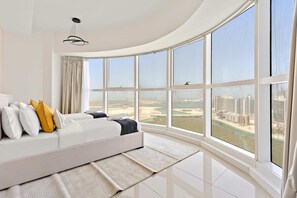 A modern bedroom with a curved ceiling, a large window offering a view of a cityscape, a white sofa with cushions, and a hanging light fixture. - Silkhaus Premier 2BR Apartment in Marina Bay (Abu Dhabi)