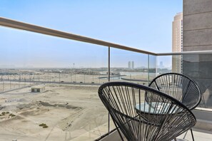 Ein Balkon mit zwei schwarzen Drahtstühlen, freier Blick auf eine Wüstenlandschaft und einen entfernten Stadt-Horizont.