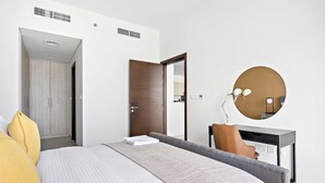 Quarto moderno com cama, mesa de cabeceira, espelho e porta que dá para outro cômodo.