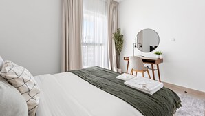 Un dormitorio moderno con una cama, un escritorio, una silla, un espejo y una ventana con cortinas.
