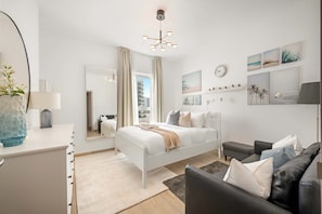 Ett modernt sovrum med en vit säng, en svart lädersoffa och en stor spegel.