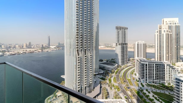 Un immeuble de grande hauteur au design moderne, situé près d’un plan d’eau, entouré d’autres immeubles imposants et d’un quartier urbain bien aménagé.