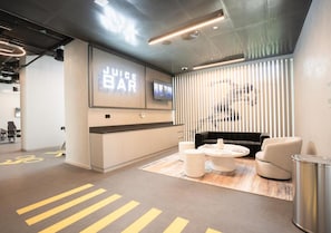 A modern lounge area with a reception desk, seating, and a large screen displaying 'JUICE BAR'. - Silkhaus Luxury 2bdr Dubai Creek Harbour (Dubai)