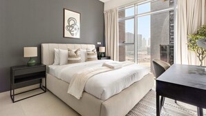 A modern hotel room with a large bed, a bedside table with a lamp, a view of the city through large windows, and a dining table. - Silkhaus Executive 1bdr Reem Island Najmat (Abu Dhabi)