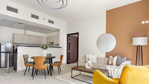 A modern living room with a yellow armchair, a coffee table, and a sofa. There is a dining area with chairs and a table, and a kitchen in the background. - Silkhaus Executive 1bdr Reem Island Najmat (Abu Dhabi)