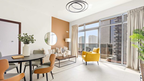 A modern living room with a sofa, coffee table, and chairs, a dining area with a table and chairs, and large windows with a city view. - Silkhaus Executive 1bdr Reem Island Najmat (Abu Dhabi)