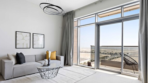 Una sala de estar moderna con un sofá gris, una mesa de centro y vistas a un paisaje desértico a través de amplios ventanales.