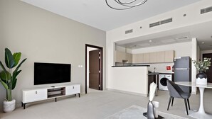 Una sala de estar moderna con un televisor de pantalla plana, un comedor con una mesa redonda y una cocina al fondo.