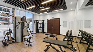 Un gimnasio con diversos equipos de ejercicio, piso de madera y ventanas amplias.