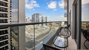 Un balcón con mesa y sillas, con vistas a un paisaje urbano que incluye edificios modernos y una autopista.