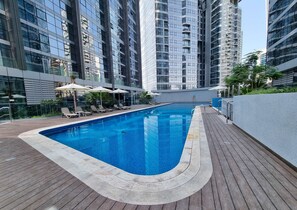 Ein moderner Pool auf dem Dach mit Liegestühlen und Sonnenschirmen, umgeben von Hochhäusern.