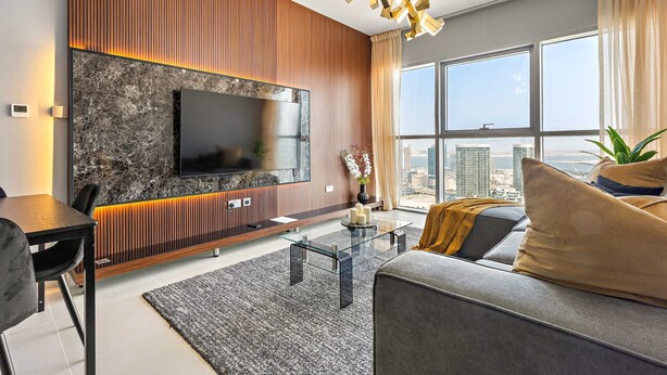 Ein modernes Wohnzimmer mit einem großen Flachbildfernseher, einem Glastisch, einer Couch und Blick auf die Stadt durch große Fenster.