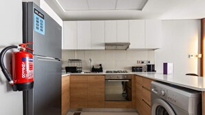 Eine moderne Küche mit integrierter Waschmaschine und Trockner, einem Edelstahlkühlschrank und einem an der Wand befestigten Feuerlöscher.