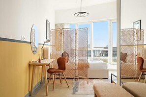 A hotel room with a bed, a desk, a chair, a window with a view, and a partition with a mesh design. - Silkhaus Chic Studio Barsha Heights Madison (Dubai)