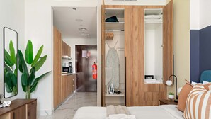 A hotel room with a bed, a wooden wardrobe, a small desk, a mirror, and a potted plant. - Silkhaus New Tower Near Al Reem Adgm (Abu Dhabi)