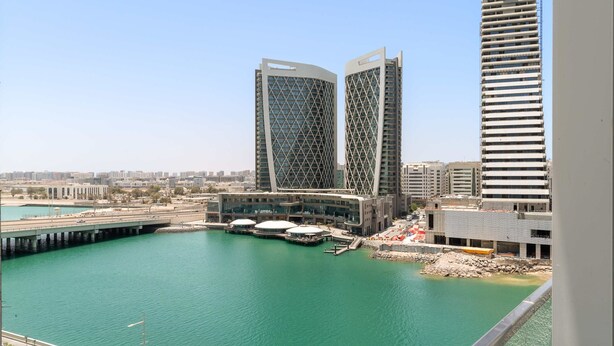 A waterfront view with modern buildings, a bridge, and a marina. - Silkhaus New Tower Near Al Reem Adgm (Abu Dhabi)