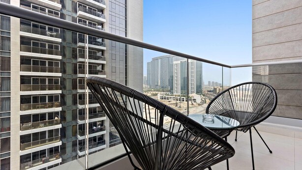 A balcony with two black wireframe chairs and a glass table, overlooking a cityscape with modern buildings. - Silkhaus Spacious 1BR Najmat Reem Island (Abu Dhabi)