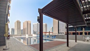 An outdoor swimming pool with lounge chairs, a pergola, and a cityscape view. - Silkhaus Spacious 1BR Najmat Reem Island (Abu Dhabi)