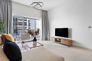 Ein modernes Wohnzimmer mit einer Couch, einem Couchtisch, einem Fernseher und einem großen Fenster mit Vorhängen.