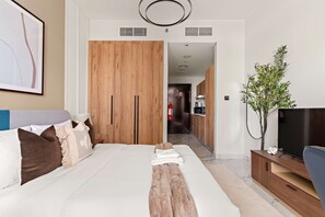 A modern hotel room with a large bed, wooden wardrobe, a television, and a small plant. - Silkhaus Chic Studio Shared Pool and Gym (Abu Dhabi)