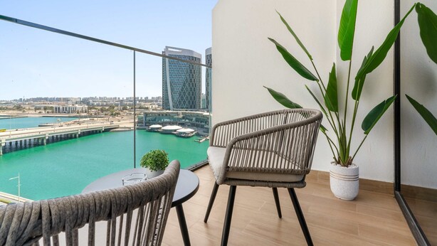 Un balcon donnant sur une marina et des immeubles, une chaise en osier, une petite table et un pot de fleurs.
