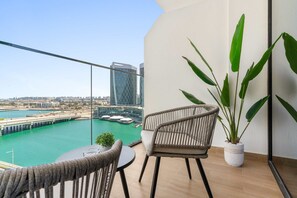 Ein Balkon mit Blick auf einen Hafen und Gebäude, ein Korbstuhl, ein kleiner Tisch und ein Blumentopf.