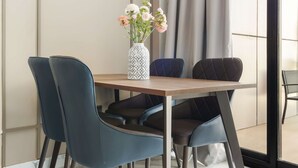 Un coin repas avec une table en bois, quatre chaises bleues et un vase blanc orné de fleurs.