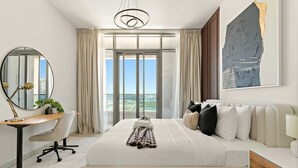 Une chambre d’hôtel avec un grand lit, un bureau, une chaise, un miroir, une fenêtre avec des rideaux et un tableau au mur.