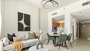 Un salon moderne avec un canapé, une table basse et des fauteuils. On aperçoit une cuisine au fond.