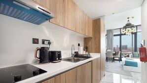 Ett modernt kök med en inbyggd spis, kaffebryggare och diskho. Här finns också en matplats med ett bord och stolar, och genom de stora fönstren har man utsikt över staden.