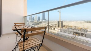 Ein Balkon mit einer Holzbank und einem Glastisch, mit Blick auf eine Stadtlandschaft mit Gebäuden und einer Baustelle.