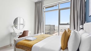 Une chambre d’hôtel avec un grand lit, un bureau, une chaise, un miroir et une vue sur la ville grâce à de grandes fenêtres.