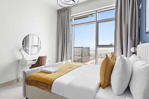 Ein Hotelzimmer mit einem großen Bett, einem Schreibtisch, einem Stuhl, einem Spiegel und Blick auf die Stadt durch große Fenster.