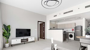 Un salon moderne avec un téléviseur à écran plat, un meuble de rangement blanc, une table basse ronde et une grande plante en pot.