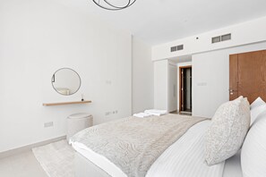 A modern bedroom with a bed, a round mirror, a wooden shelf, and a door leading to another room. - Silkhaus Julphar Tower By Al Fay Park Al Reem (Abu Dhabi)