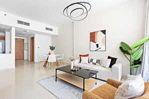 A modern living room with a black coffee table, white sofa, and a large green plant. - Silkhaus Julphar Tower By Al Fay Park Al Reem (Abu Dhabi)