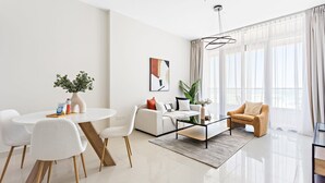 A modern living room with a white sofa, a round dining table with chairs, a coffee table, and a large window with sheer curtains. - Silkhaus Julphar Tower By Al Fay Park Al Reem (Abu Dhabi)