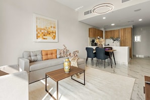 A modern living room with a sofa, coffee table, and a dining area with chairs and a kitchen in the background. - Silkhaus Luxury 3bdr Stay in Maryah Island (Abu Dhabi)