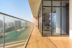 A modern balcony with glass railings, a wooden floor, and a view of a cityscape and water body. - Silkhaus Luxury 3bdr Stay in Maryah Island (Abu Dhabi)